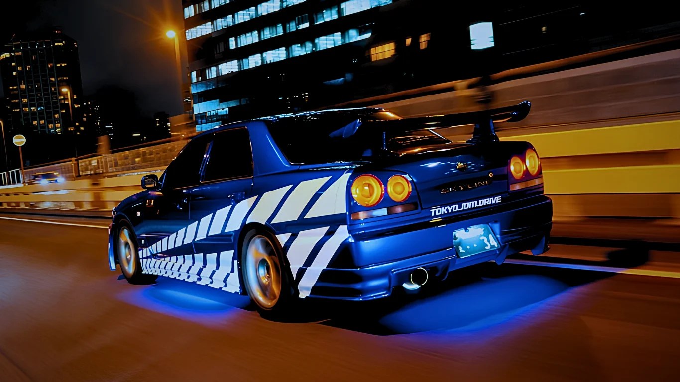 A Nissan Skyline R34 driving along an elevated expressway at night, with lit office towers behind